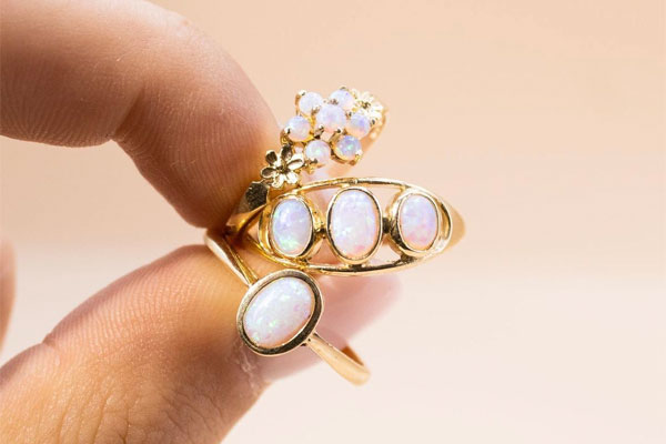 Three Opal rings being held between a thumb and a forefinger