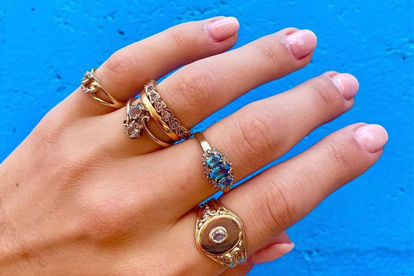 A hand with a selection go pre-loved rings including a signet on the pointing finger, a topaz cluster on the middle finger and a gold stacking ring on the pinky finger